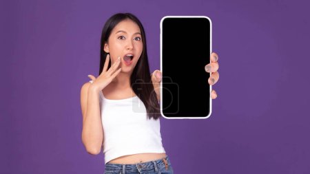 Téléchargez les photos : Full body length photo portrait of beautiful Asian young woman ,Excited surprised girl showing big smart phone with blank screen , white screen isolated on purple background , Mock Up Image - en image libre de droit