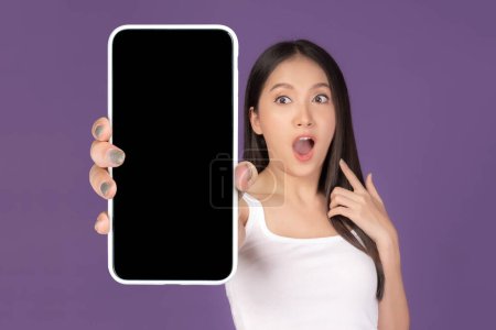 Téléchargez les photos : Beautiful Asian young woman ,Excited surprised girl showing big smart phone with blank screen , white screen isolated on purple background , Display Mock Up Image - en image libre de droit