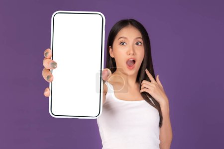 Photo for Beautiful Asian young woman ,Excited surprised girl showing big smart phone with blank screen , white screen isolated on purple background , Display Mock Up Image - Royalty Free Image