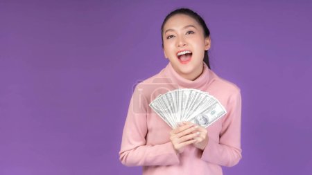 Photo for Successful beautiful Asian business young woman holding money US dollar bills in hand isolated on purple background with copy space , business concept - Royalty Free Image