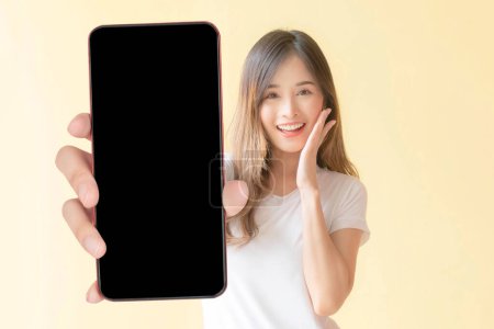 Téléchargez les photos : Belle asiatique jeune femme montrant grand téléphone intelligent avec écran blanc, écran noir vide espace de copie pour la bannière publicitaire isolé sur fond jaune, image factice - en image libre de droit