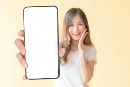 Téléchargez les photos : Belle Asiatique jeune femme montrant grand téléphone intelligent avec écran blanc, écran blanc vide espace de copie pour la bannière publicitaire isolé sur fond jaune, Mock Up Image - en image libre de droit