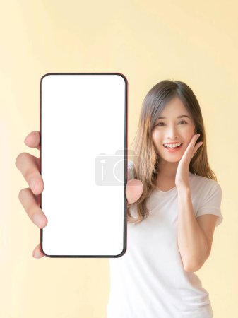 Téléchargez les photos : Belle Asiatique jeune femme montrant grand téléphone intelligent avec écran blanc, écran blanc vide espace de copie pour la bannière publicitaire isolé sur fond jaune, Mock Up Image - en image libre de droit