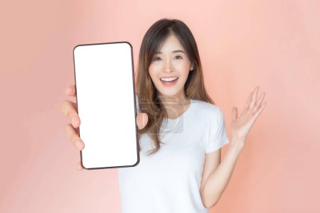 Téléchargez les photos : Belle Asiatique jeune femme montrant grand téléphone intelligent avec écran blanc, écran blanc vide espace de copie pour la bannière publicitaire isolé sur fond rose, Mock Up Image - en image libre de droit
