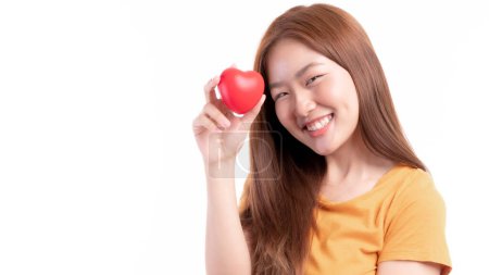 Téléchargez les photos : Portrait de sourire une belle jeune femme asiatique tenant le cœur rouge à la main sur fond blanc concept Saint-Valentin - en image libre de droit