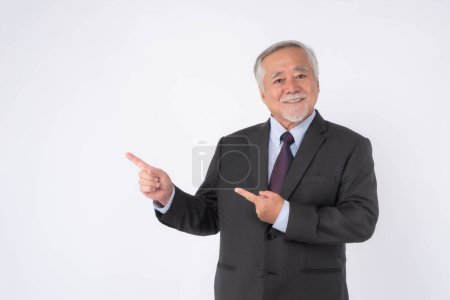Foto de Hombre de negocios sénior asiático, hombre viejo con traje se siente feliz buena salud señalando el dedo al espacio de copia vacío para el producto actual o espacio en blanco para la publicidad aislada en el fondo blanco - Imagen libre de derechos