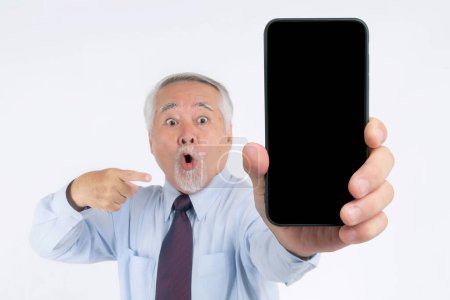 Téléchargez les photos : Homme d'affaires asiatique senior, vieil homme avec costume se sentent heureux pointant du doigt vers un grand téléphone intelligent avec écran blanc, écran noir isolé sur fond blanc - écran vide de téléphone intelligent Mock Up Image - en image libre de droit
