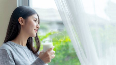 Belle beauté femme asiatique mignonne fille se sentent heureux boire du lait pour une bonne santé le matin, profiter du temps dans son fond de chambre à coucher blanche à la maison - concept de beauté de style de vie femme