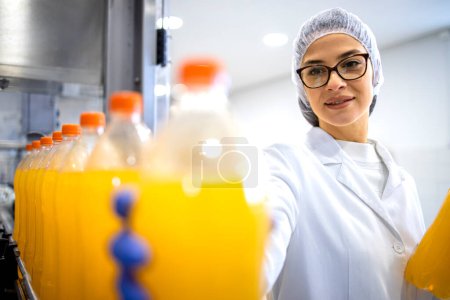 Bottling factory interior and female worker checking orange juice production.