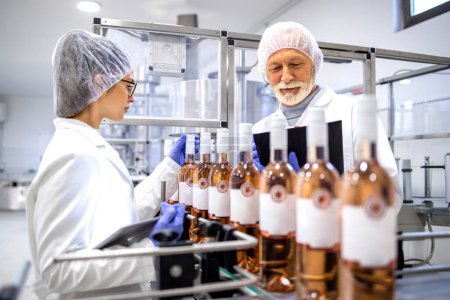 Foto de Working together controlling bottled wine production in factory. - Imagen libre de derechos