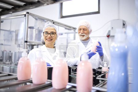 Foto de Felices trabajadores de la fábrica sonrientes produciendo champú y jabón líquido para la industria de limpieza. - Imagen libre de derechos