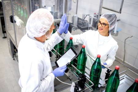 Production line workers celebrating success inside bottling factory for PET packaging.