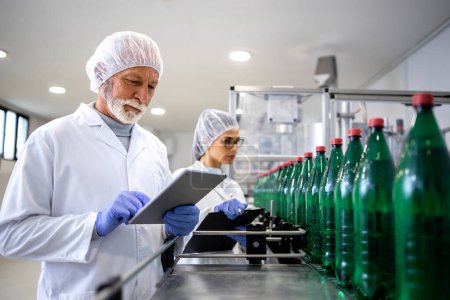 Concentrated quality control workers controlling production of bottled drinking water in beverage factory.