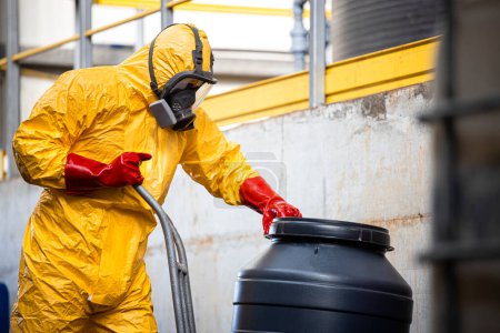 Téléchargez les photos : Travailleur chimique en combinaison de protection et masque à gaz travaillant avec des matières dangereuses et des déchets toxiques dans l'usine de production. - en image libre de droit