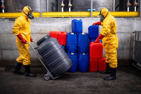 Téléchargez les photos : Chemical plant workers in protection suit handling barrels and canisters with chemicals inside production factory. - en image libre de droit