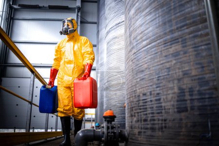Téléchargez les photos : Travailleur en combinaison de protection et masque à gaz travaillant dans une usine chimique et transportant des substances dangereuses. - en image libre de droit
