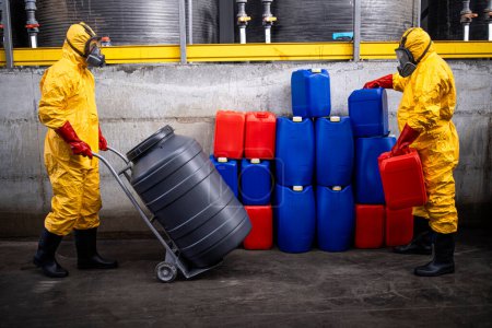 Téléchargez les photos : Travailleurs de l'usine de production chimique déplaçant des barils et des conteneurs avec des matières acides ou dangereuses. - en image libre de droit