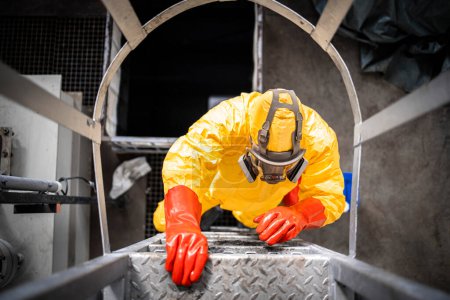 Téléchargez les photos : Vue du dessus du travailleur en combinaison de protection et masque à gaz escalade échelle industrielle métallique à l'intérieur de l'usine de produits chimiques. - en image libre de droit