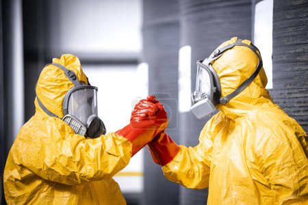 Trabajadores químicos en traje de protección, máscara de gas y guantes celebrando el éxito en el trabajo.