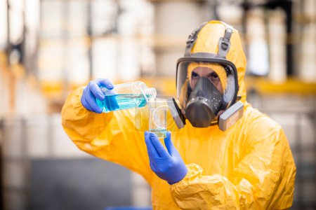 Téléchargez les photos : Travailleur de contrôle de qualité en combinaison de protection et masque à gaz testant la qualité des produits chimiques à l'intérieur de l'usine de production chimique . - en image libre de droit