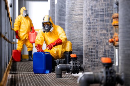 Téléchargez les photos : Fully protected workers in yellow hazmat suit, gas masks and gloves handling dangerous chemicals or substances. - en image libre de droit