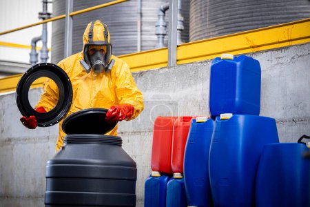Téléchargez les photos : Travailleur expérimenté en combinaison de protection et masque à gaz ouvrant des barils avec de l'acide à l'intérieur de l'usine de production chimique. - en image libre de droit