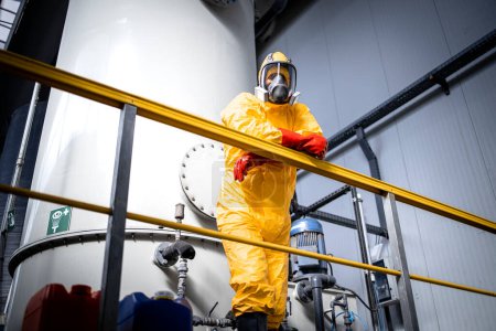 Téléchargez les photos : Portrait of factory worker in protective yellow suit, gas mask and gloves leaning against the fence inside chemicals production plant. - en image libre de droit