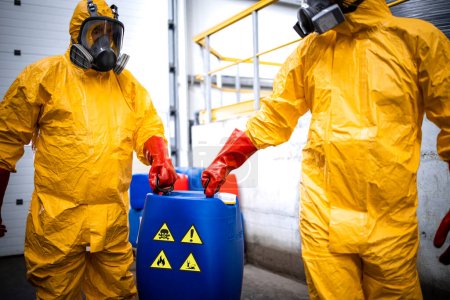 Fábrica de producción de químicos. Trabajadores experimentados completamente protegidos en máscara de gas que transportan residuos peligrosos y tóxicos en planta química.