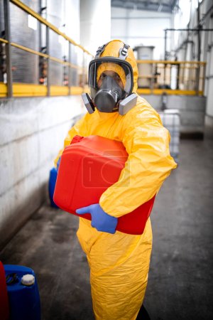 Portrait of chemicals production plant worker in protective suit and gas mask holding plastic can with chemical.