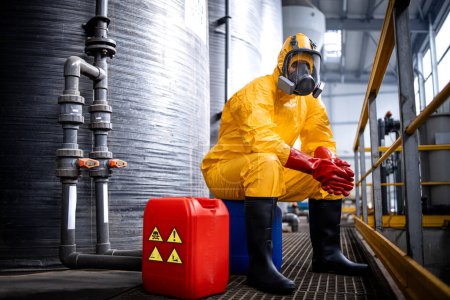 Photo for Portrait of experienced factory worker in protective suit and gas mask having a break inside chemicals and acid production plant. - Royalty Free Image