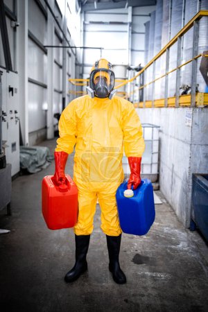 Téléchargez les photos : Portrait d'un ouvrier d'usine portant une combinaison de protection et un masque à gaz transportant des produits chimiques dans une usine de production industrielle. - en image libre de droit