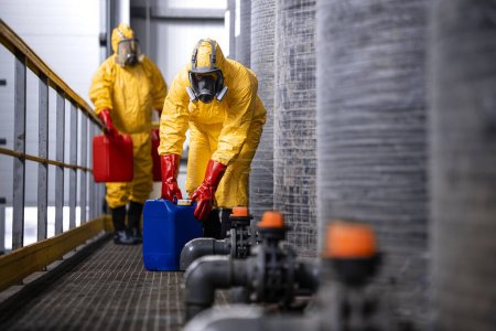 Téléchargez les photos : Experienced and trained workers with gas masks handling dangerous material inside chemicals factory. - en image libre de droit