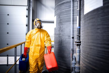 Téléchargez les photos : Factory worker in yellow hazmat suit walking by acid tanks in chemicals factory. - en image libre de droit