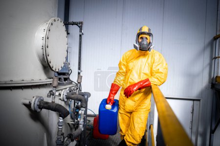 Téléchargez les photos : Portrait d'ouvrier d'usine en combinaison jaune protectrice, masque à gaz et gants appuyés contre la clôture à l'intérieur de l'usine de production de produits chimiques. - en image libre de droit