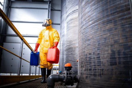 Photo for Chemicals production industry interior and worker in protection suit and gas mask walking by acid tanks. - Royalty Free Image