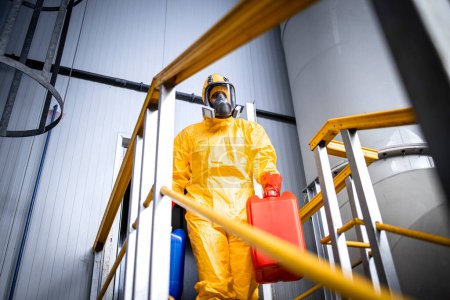 Téléchargez les photos : Factory worker wearing protective suit and gas mask carrying chemicals through industrial production plant. - en image libre de droit