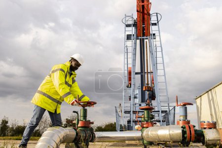 Photo for Oil field worker closing industrial valve by the oil rig controlling production. - Royalty Free Image