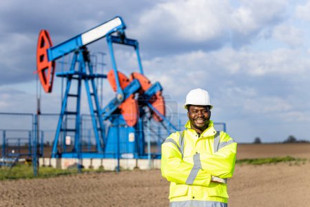 Photo for Portrait of American oil field worker in protective work wear proudly standing in front of the oil rig. - Royalty Free Image