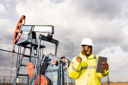 Photo for Oil production industry. Oil field workman in protection equipment looking at digital tablet and celebrating success. - Royalty Free Image