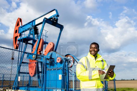 Photo for Oil filed supervisor with tablet computer standing by the pump jack and checking crude oil production. - Royalty Free Image