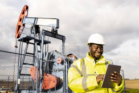 Photo for Oil filed worker standing in front of the oil rigs and using his digital tablet computer. - Royalty Free Image