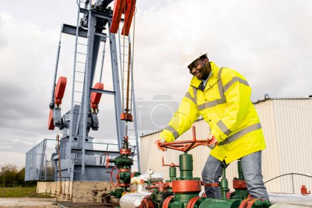 Photo for Oil field worker closing pipeline valve. In background oil rig producing crude oil. - Royalty Free Image