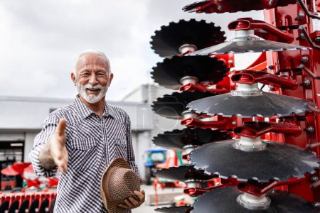 Téléchargez les photos : Portrait de fermier âgé heureux achetant des machines et des outils agricoles tels que herse. - en image libre de droit