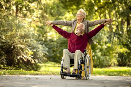 Positive Senioren im Rollstuhl mit erhobenen Armen fühlen sich glücklich und lebendig. Lebens- und Krankenversicherung.