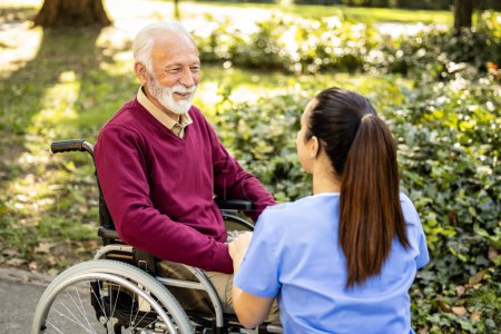 Téléchargez les photos : Assistante infirmière prenant soin d'un homme âgé en fauteuil roulant. - en image libre de droit