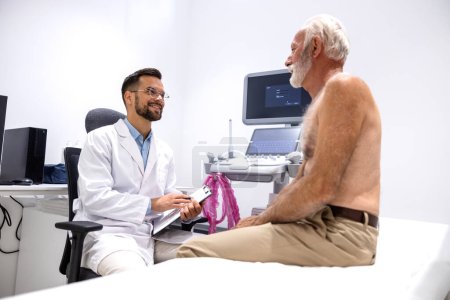 Téléchargez les photos : Médecin et patient âgé torse nu ayant une conversation avant l'examen échographique. - en image libre de droit