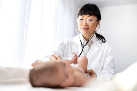 Experienced female pediatrician doctor checking baby's heartbeat with stethoscope and examining overall health.