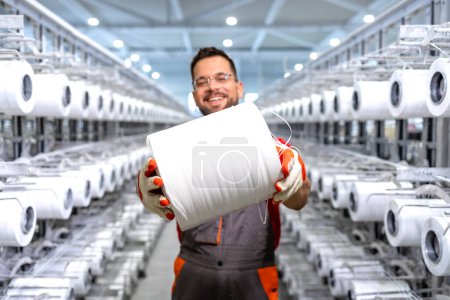 Photo for Experienced textile factory worker holding thread spool and and standing by industrial knitting machine. - Royalty Free Image