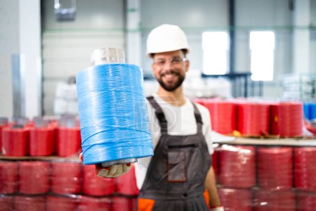 Textile factory worker holding thread spool and smiling.