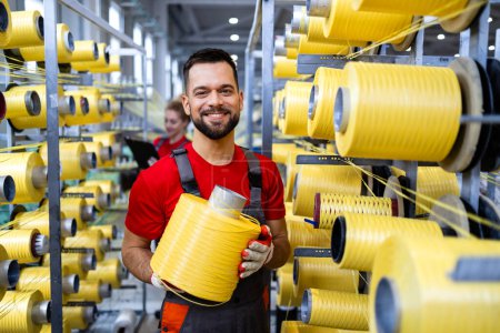 Photo for Portrait of textile industry worker holding thread spool by knitting machine. - Royalty Free Image